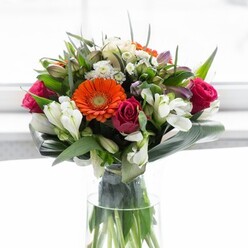 A testament to Brentwood's signature floristry, this exquisite bouquet embodies a masterful balance of structure, colour, and emotion. Creamy gerberas form a luminous border, their gentle petals encircling brilliant orange centres that glimmer like lanterns illuminated by late afternoon sun along Shenfield Road. Deep fuchsia roses, bold and elegantly furled, bring richness and classic allure, while ivory lilies and clusters of petite white blooms interweave, adding layered freshness evocative of early spring walks through Hartswood. Glossy, broad leaves are artfully shaped at the bouquet's base, creating a protective, verdant collar that stabilises and showcases the effervescent colours. Between the blooms, sprigs of fine greenery infuse the ensemble with contrasting texture and a sense of abundance. The arrangement glows beneath a gentle, diffuse light, highlighting every intricate detail without overpowering the bouquet's quiet beauty. There's an underlying fragrance-hints of rose and lily mingling with the clarity of freshly snipped foliage-suggesting tranquillity and celebration in the heart of Brentwood. Ideal for a thoughtful housewarming, gathering of friends, or commemorating a new beginning, each flower sings with optimism and the promise of cherished local connections.